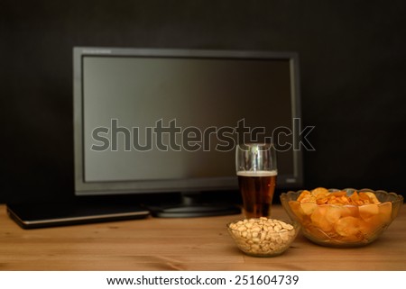 TV and computer with unhealthy snack on table isolated on black background - stock photo