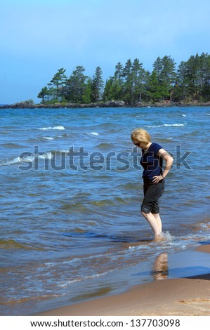 Woman rolls up her jeans and wades in the cool waters of Lake Superior in Upper Peninsula Michigan.