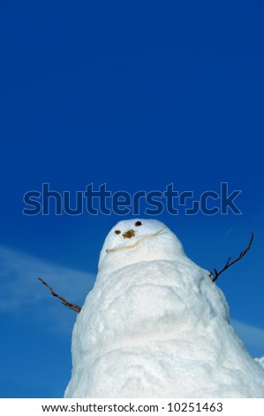 Big blue sky frames a snowman.  Sticks for arms and stones for eyes.  Low angle shot.