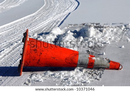 Snow storm brings on hazardous road conditions.  Fallen orange traffic cone lays besides snow covered highway.