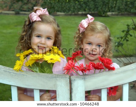 Sisters stand by white, wooden garden gate.  They have picked bouquets for their mom.