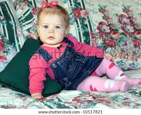 Young infant leans on her arm modeling a denim overall jumper and hot pink shirt.