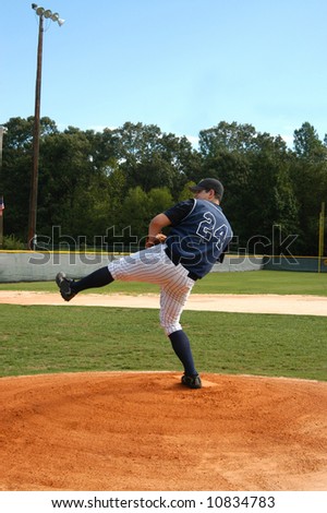 Young male baseball player winds up for the pitch.  Navy and white uniform.  Blue skies and baseball field.
