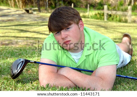 Golf game over, teen lays on grass resting.  Sunshine and bright skies.  Golf club rests through his arms.