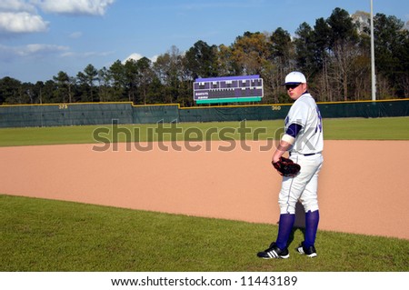 Baseball player pauses during game to look back over his shoulder.  Scoreboard in background.