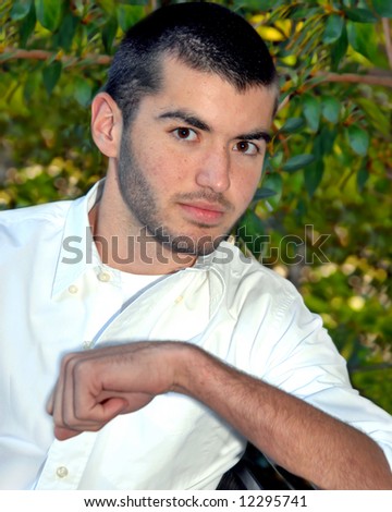 Brown eyes and dark haired, male teen is wearing white shirt in garden setting.