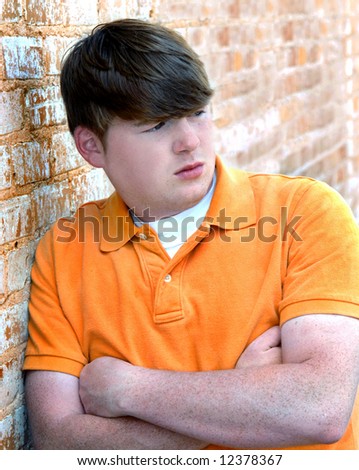 Brick building serves as shoulder rest for young male teen.  Orange brick and orange polo shirt.