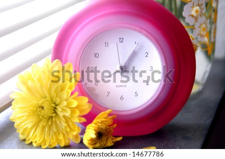 Bright light from window shows time on a hot pink retro clock sitting on window ledge.  Yellow chrysanthemums sit at base.