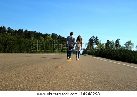 Teens walk down middle of country road.  Holding hands they face a bright future together as friends.