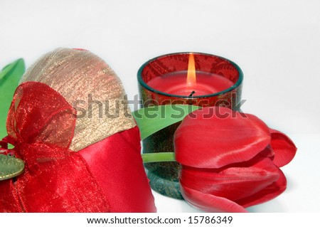 Burning red candle sits behind a single long stemmed tulip.  Puffy red heart is in foreground.