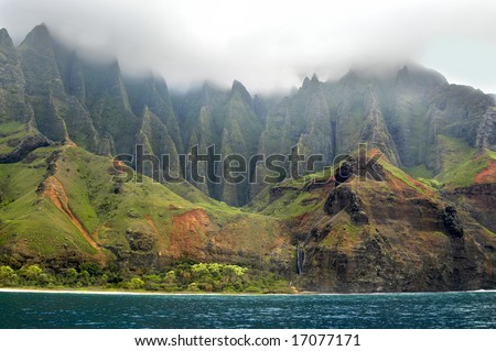 Aqua waters hug the coastline of the Na Pali Coast on Kauai, Hawaii.  Lush green ridges disappear into the clouds.