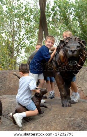 Four young boys at zoo ride the bronze sculpture of a lion and cub.