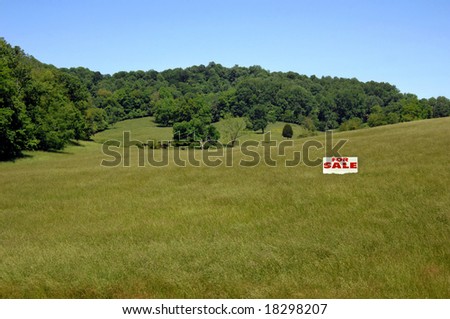 Acreage for sale in the mountains of Tennessee.  Lush green grass and blue skies.  Sign in middle of field.