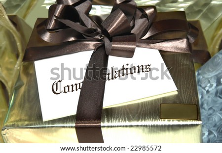 Gold wrapped package is tied with brown ribbon.  White envelope attached has the word \