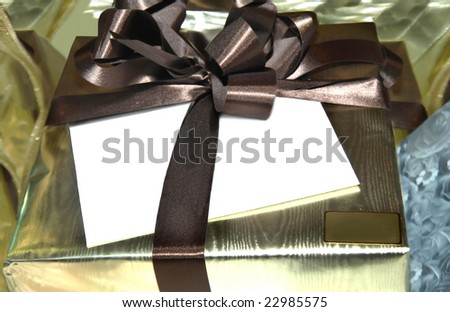 Gold wrapped package is tied with brown ribbon.  Blank white envelope sits under ribbon.  Small square can be personalized.