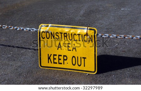 Construction sign warns of potential danger at construction site.  Yellow sign hangs from long metal chain.