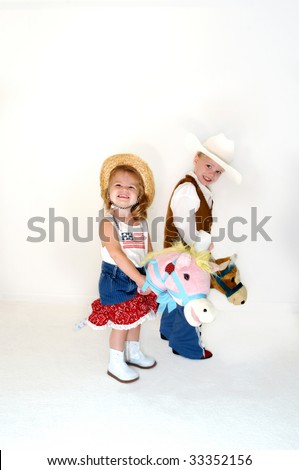 Brother and sister saddle up for a little fun.  Both are dressed in western wear and astride stick ponies.