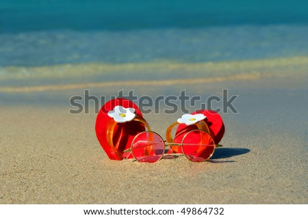 Tiny red flip flops, decorated with white daisies, sit in the sand alongside pink tinted sunglasses.  Ocean waves wash the sands.  Also a Metaphor for \