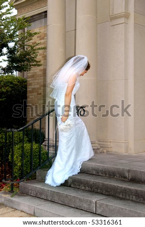 Bride climbs steps at church on the day of her wedding.  Dressed in slender fitting strapless dress, her head is down in contemplation.