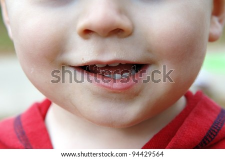 Baby\'s face is dirty and he is giving a lop-sided grin.  Baby teeth show in his mouth.