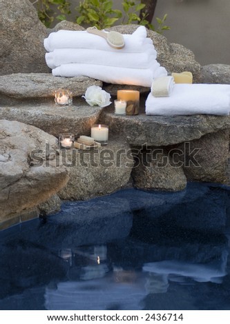 spa setting with towels and candles and soaps and loofah sponge with reflections from water