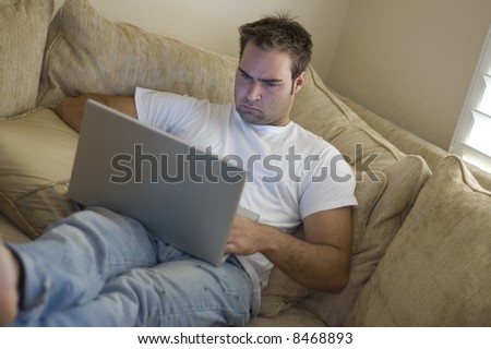 young man laying on sofa using laptop computer