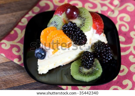 A slice of cheese cake on a black plate garnished with assorted fruit.