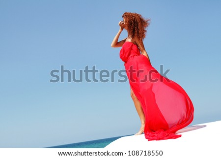young beautiful woman in red dress isolated over blue sky background