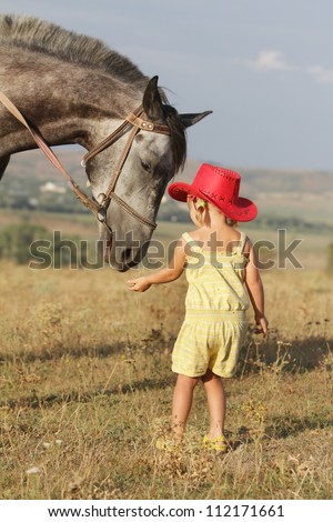 young girl feeding horse on natural background