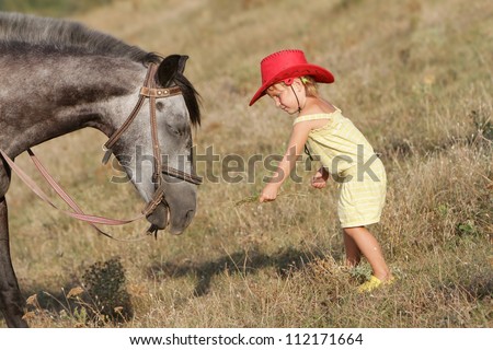young happy child girl feeding horse on natural background