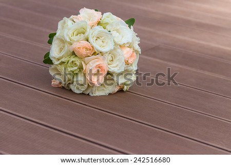 Wedding bouquet of peach and white roses lying on wooden floor
