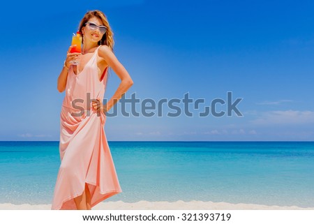 outdoor portrait of young smiling beautiful woman with bright cocktail on tropical sand beach