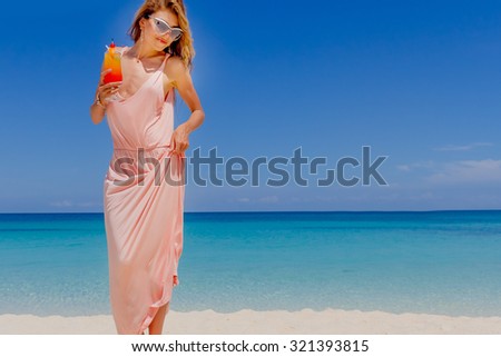 outdoor portrait of young smiling beautiful woman with bright cocktail on tropical sand beach