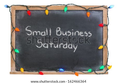 Small Business Saturday written in white chalk on a black chalkboard surrounded by festive colorful lights isolated on white