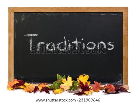Traditions written in white chalk on a black chalkboard surrounded with fall leaves isolated on white