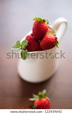 Fresh strawberry in cup on wooden tabletop with red string lights in background