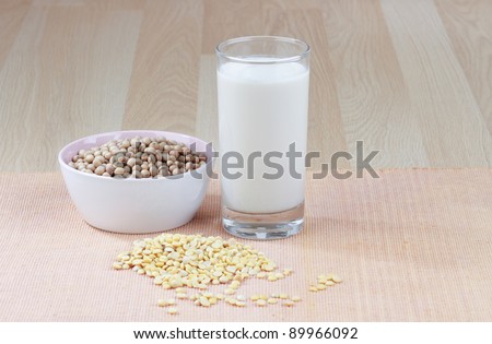 A glass of soy milk with a bowl of raw soybean and soybean seed