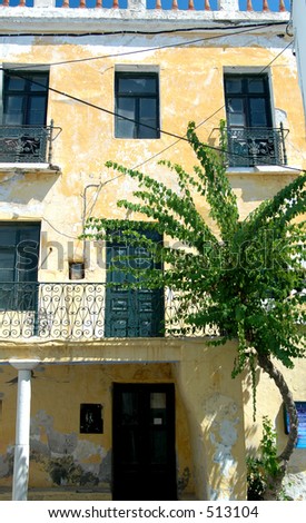 an old building in the greek islands with beautiful doors and intricate wrought iron railings and a tree growing through the street