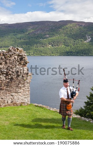 URQUHART CASTLE, UNITED KINGDOM - AUGUST 13: Scottish Highlander wearing kilt and playing Bagpipe at Urquhart Castle, on August 13, 2013. The Castle sits beside Loch Ness in the Highlands of Scotland.