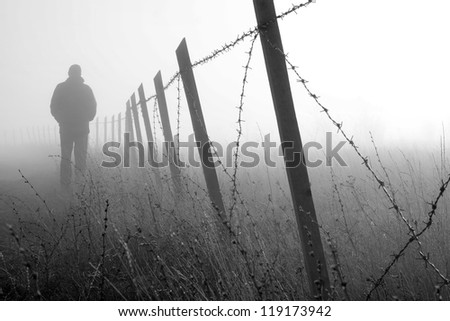 Man walking near barbed wire fence in dense fog