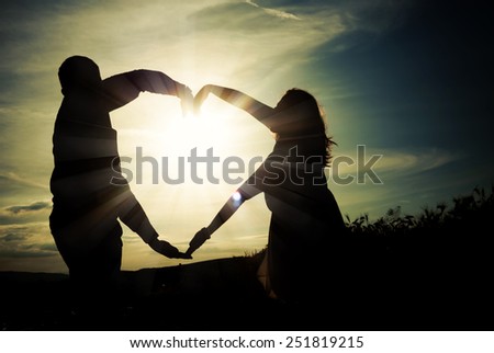 Silhouette of loving couple holding hands in heart shape over orange sunset background - vintage phot