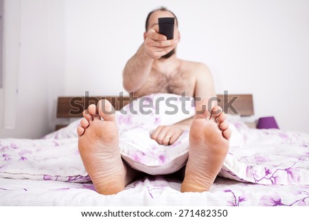 Man watching TV from the bad - focus on the feet