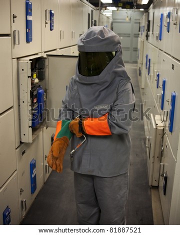 An Electrical worker wearing arc-flash protection.  The tool in his hand is used to draw out a large circuit breaker.