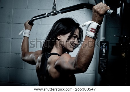 Woman doing pull-ups on a machine in the gym - exercising lifting dumbbells