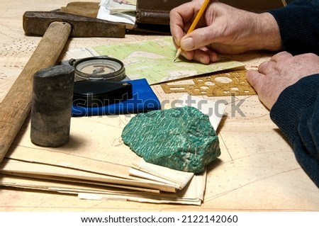 Geologist works with maps. On his desk are: map case, geological hammer, compass, magnifying glass, drill core, rock samples, topographic and geological maps Foto stock © 