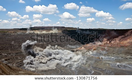 excavators,trucks and heavy machinery in open cast mine after blast among dust and smoke