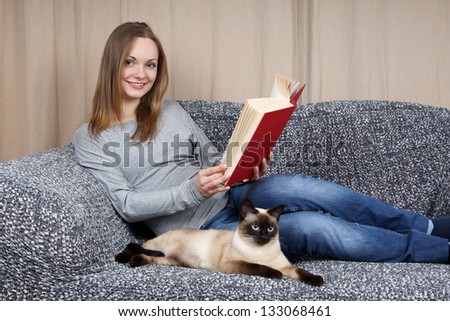 young woman relaxing with a book and her cat on the couch