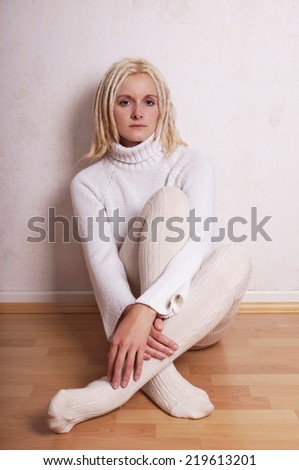 lonely woman wearing turtleneck sweater and overknee socks sitiing on floor leaning against wall