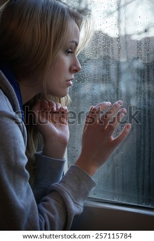 sad young woman looking through window with raindrops
