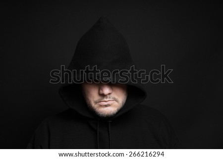 man wearing black hoodie hiding eyes in the dark